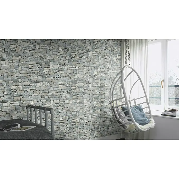 Rasch Vliestapete - Grau, Steinoptik, 10,05 x 0,53 m - Helle Inneneinrichtung mit einer Steinwand und einem schwebenden Rattansessel mit weichen Kissen, die für Gemütlichkeit sorgt.
