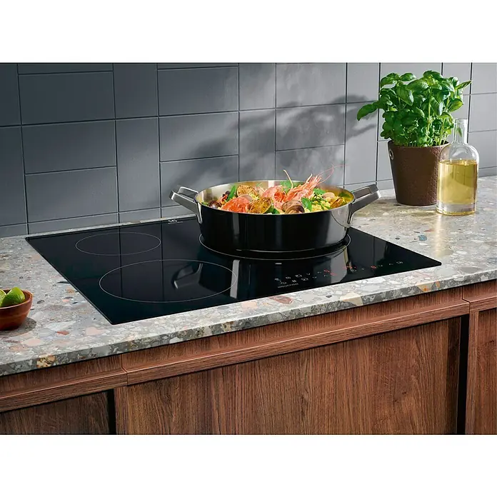Electrolux Placa de cocción LIT60336C - Número de fogones de inducción: 3 ud. - Una placa de cocción negra de Electrolux exhibe una olla llena de comida, complementada con utensilios de cocina y elementos decorativos.