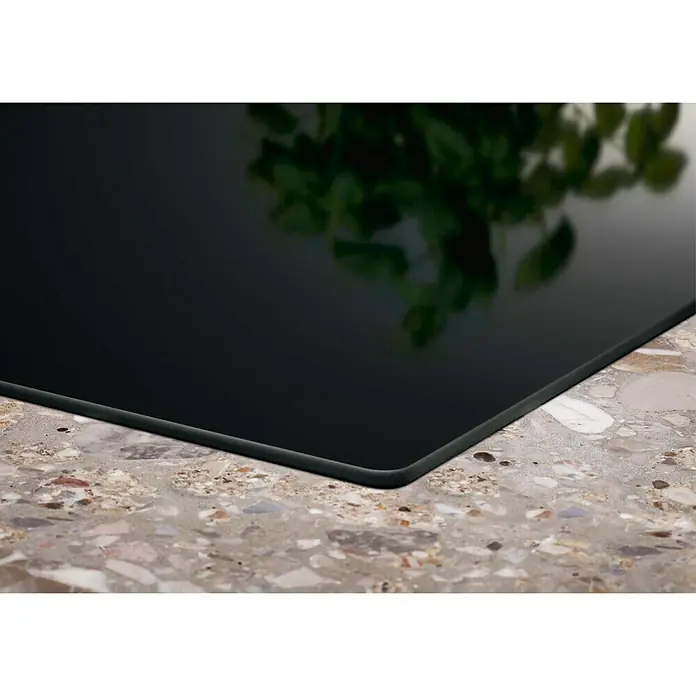 Electrolux Placa de cocción LIT60336C - Número de fogones de inducción: 3 ud. - Primer plano de una placa de inducción negra sobre una encimera de terrazo, que muestra una adición elegante y moderna a cualquier cocina.