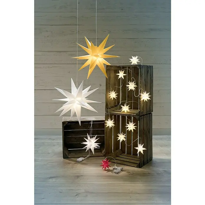 Tween Light LED-Stern 3D Kunststoff hängend - 50 cm, Weiß, Lichtfarbe: Warmweiß, IP44, Netzbetrieben - Helle gelbe und weiße Papiersterne hängen und liegen mit Sternenketten auf Holzschemeln und auf dem Boden, eine festliche Dekoration.