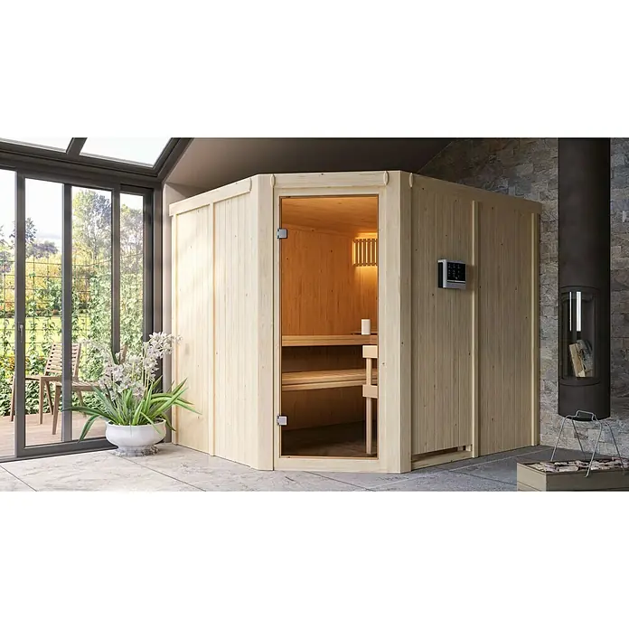 Karibu Elementsauna Horna - Mit 9 kW Saunaofen mit externer Steuerung, L x B x H: 196 x 231 x 198 cm - Ein helles Holzsauna-Interieur mit Glasfront und einer Steuerung an der Außenseite, neben einem Kamin in einem modernen Raum.