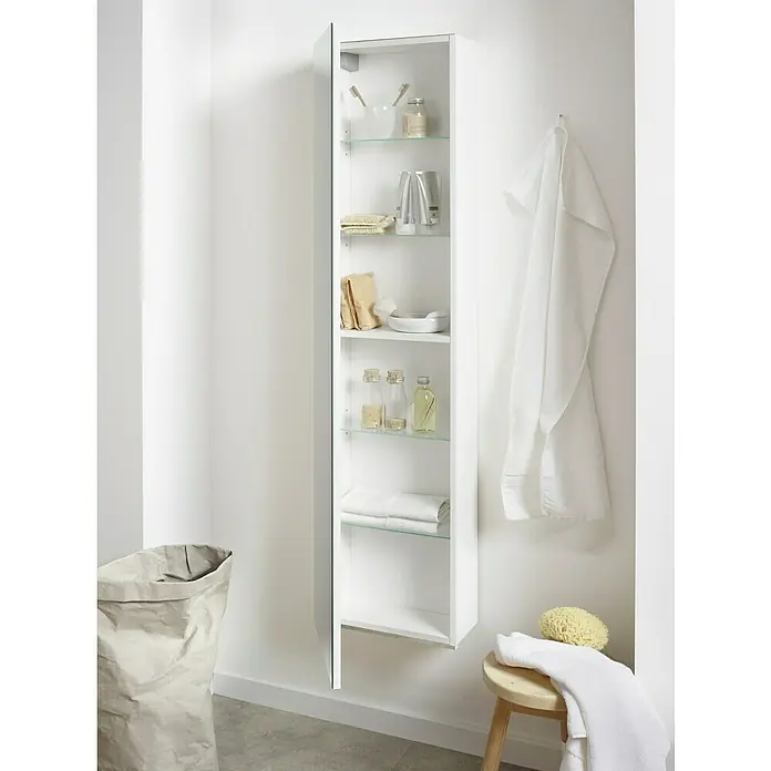 Riva Spiegel-Hochschrank Andy - 36 x 16,5 x 155 cm, Weiß - Ein offener, weißer Badezimmerschrank mit Glasböden und verschiedenen Badezimmerartikeln, neben dem ein Hocker mit Handtüchern steht.