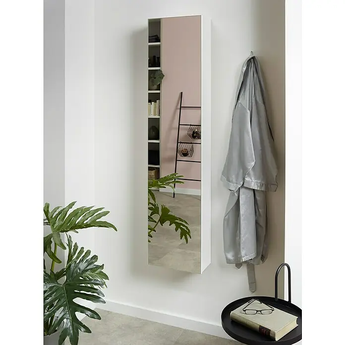 Camargue Spiegel-Hochschrank Orion - 31 x 16,5 x 147 cm, Weiß - Ein schlanker Spiegelschrank in Weiß hängt an einer weißen Wand und spiegelt ein Zimmer mit Regalen und einer Leiter wider.