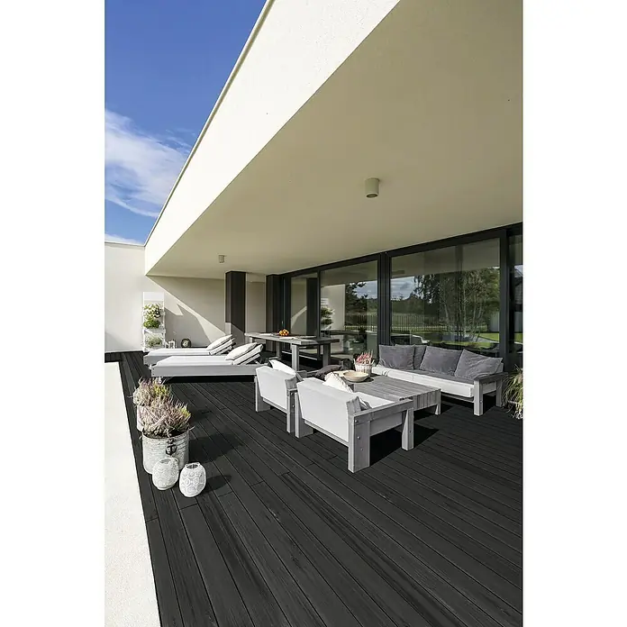 Terrassendiele - Kiefer, 250 x 14,5 x 2,8 cm, Anthrazit - Elegante Terrasse mit dunklem Holzboden und hellen Gartenmöbeln unter einem modernen Gebäudevordach.
