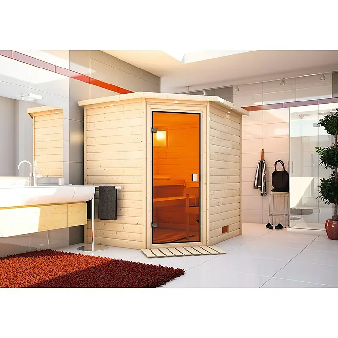 Karibu Massivholzsauna Mia - L x B x H: 184 x 224 x 202 cm, Materialspezifizierung Tür: Ganzglas Bronze, Inklusive Ofenschutzgitter, Mit Dachkranz und Beleuchtung - Das Bild zeigt eine moderne Sauna aus hellem Holz mit einer Glastür in einem Badezimmer. Einladender Rückzugsort für Wellness und Entspannung.