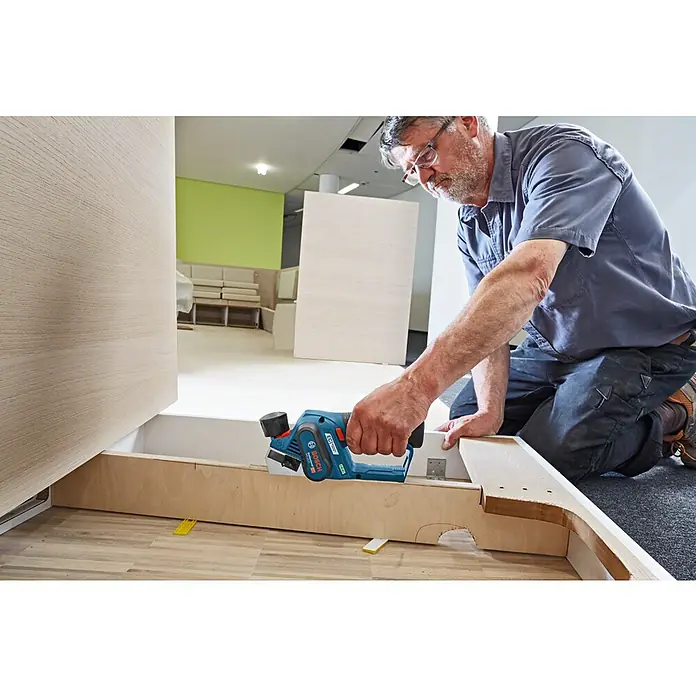 Bosch Professional Akku-Handhobel GHO 12V-20 - 12 V, Li-Ionen, Ohne Akku, Hobelbreite: 56 mm - Handwerker nutzt einen Bosch Elektrohobel, um Holz zu bearbeiten, wobei der Hobel im Fokus steht.\n