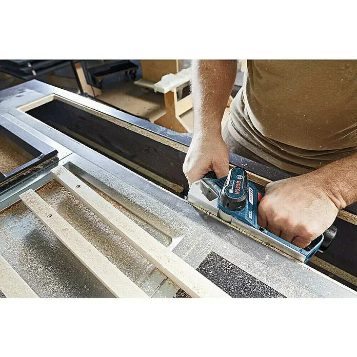 Bosch Professional Akku-Handhobel GHO 12V-20 - 12 V, Li-Ionen, Ohne Akku, Hobelbreite: 56 mm - Bosch Hobel beim Bearbeiten eines Holzstücks. Präzise Holzarbeit mit einem hochwertigen Elektrowerkzeug in einer Werkstatt.