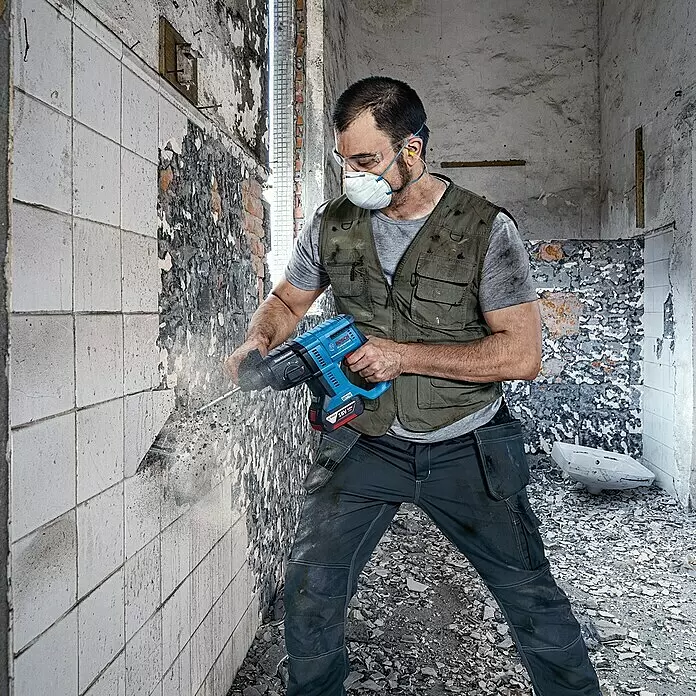 Bosch Professional AMPShare 18V Martillo combinado de batería GBH 18V-21 - 18 V, 2 baterías, 4 Ah, 2 J, Maletín incluido - Hombre usa un martillo perforador inalámbrico azul Bosch Professional para cincelar azulejos en una demolición.