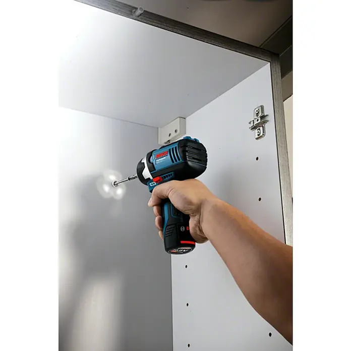 Bosch Professional Llave de impacto giratoria de batería GDR 12V-105 - 12 V, Sin batería - Un atornillador de impacto inalámbrico Bosch se utiliza para atornillar un tornillo en una tabla de gabinete blanca, lo que demuestra la potencia y versatilidad de esta herramienta.