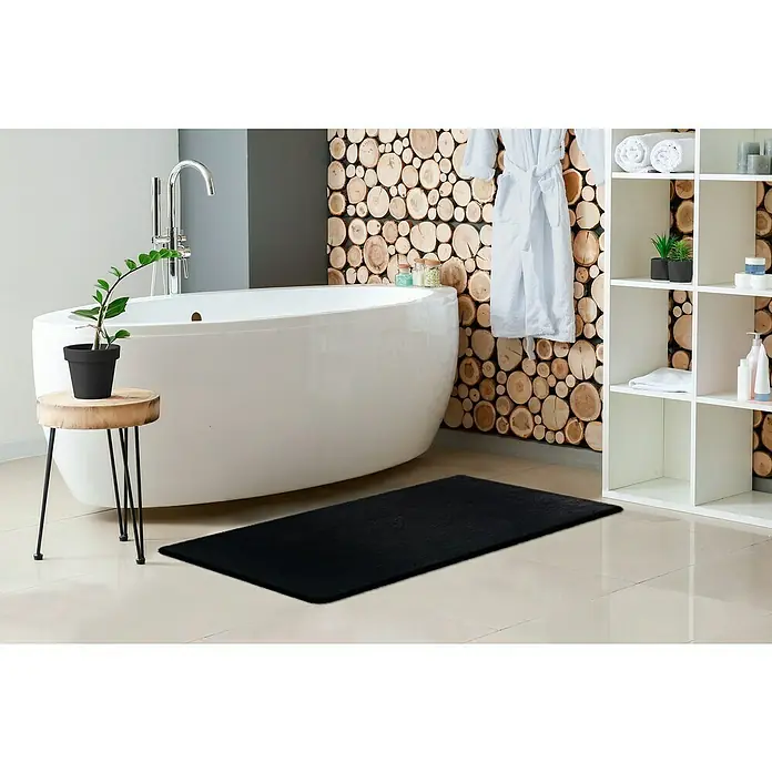 Badteppich Happy - 50 x 90 cm, Schwarz, 100% Polyester - Ein schwarzer Badteppich liegt in einem modernen Badezimmer mit weißer Badewanne und Holzdetails, der für Wärme und Komfort sorgt.