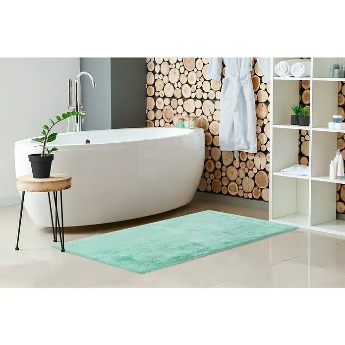 Badteppich Happy - 67 x 110 cm, Mint, 100% Polyester - Ein mintgrüner, flauschiger Teppich liegt in einem modernen Badezimmer vor einer freistehenden Badewanne.