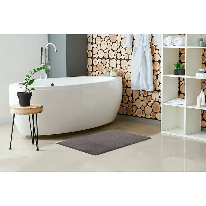 Badteppich Happy - 40 x 60 cm, Grau, 100% Polyester - Ein modernes Badezimmer mit einem weichen, grauen Badvorleger auf hellen Fliesen vor einer Badewanne und einem Regal.