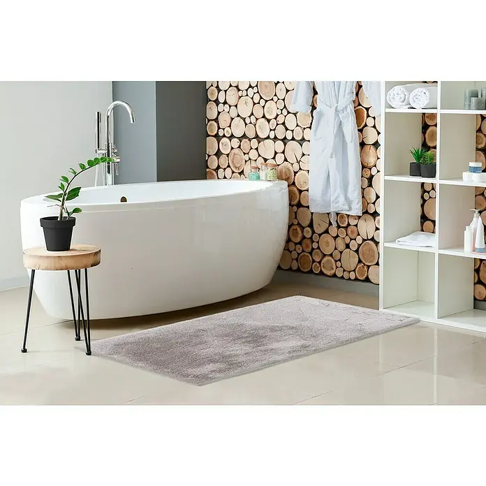 Badteppich Happy - 67 x 110 cm, Silber, 100% Polyester - Ein grauer, flauschiger Teppich liegt in einem modernen Badezimmer mit Badewanne, Holzwand und weißem Regal.