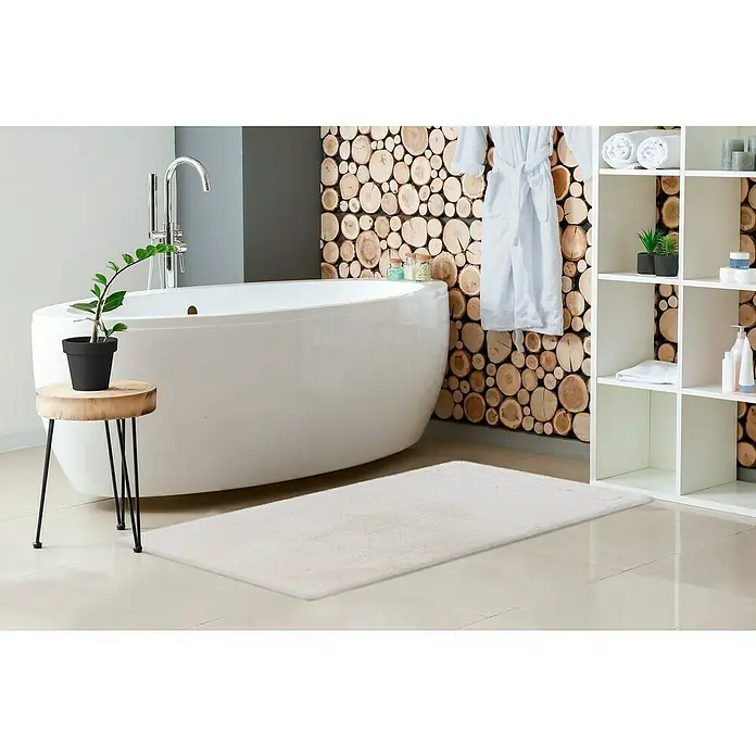 Badteppich Happy - 67 x 110 cm, Weiß, 100% Polyester - Ein Badezimmer mit einer weißen Badewanne, einem hellen Teppich und einem kleinen Beistelltisch mit einer Zimmerpflanze.