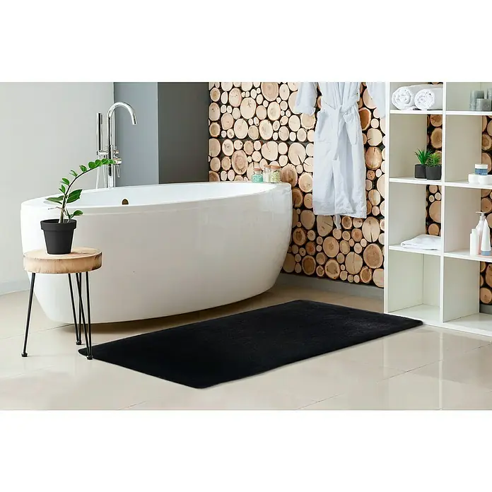 Badteppich Happy - 67 x 110 cm, Schwarz, 100% Polyester - Ein modernes Badezimmer mit einer schwarzen Badematte, einer freistehenden Badewanne und einem Holzhocker mit Pflanze.