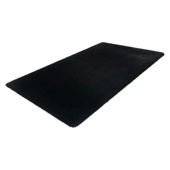 Badteppich Happy - 67 x 110 cm, Schwarz, 100% Polyester - Ein rechteckiger, schwarzer, flauschiger Teppich liegt diagonal auf einem weißen Hintergrund. Der Teppich hat eine weiche Textur und einen dichten Flor.