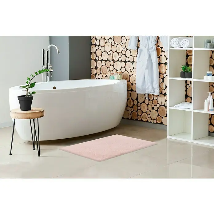 Badteppich Happy - 40 x 60 cm, Rosa, 100% Polyester - Rosa Badematte auf dem Boden neben einer Badewanne, einem Beistelltisch mit Pflanze und einem Regal.
