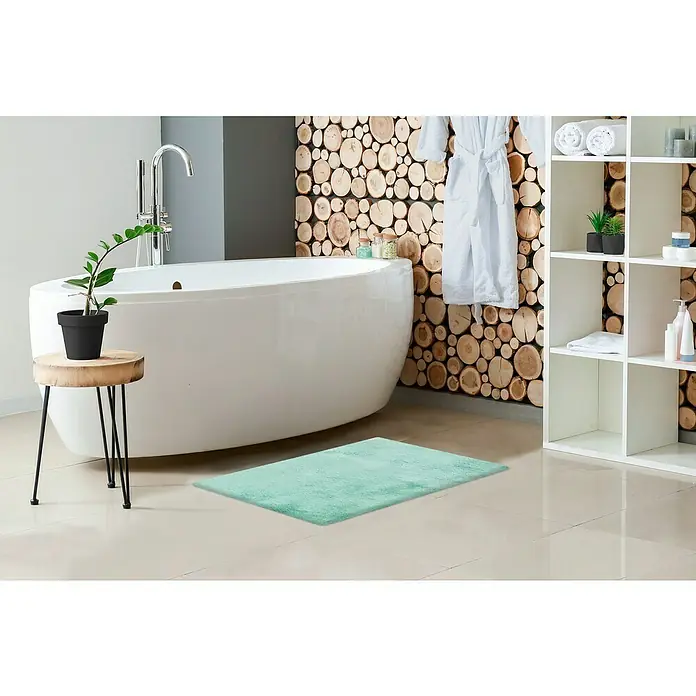 Badteppich Happy - 40 x 60 cm, Mint, 100% Polyester - Ein hellgrüner Badteppich liegt vor einer Badewanne und einem Regal mit Badutensilien, der für ein frisches Ambiente sorgt.