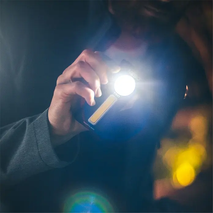 Nebo Tools Linterna Tino - 3 x 5 x 10 cm, 300 lm - Primer plano de una persona que sostiene una luz de trabajo NEBO, con un haz brillante y una base magnética para soluciones de iluminación versátiles.