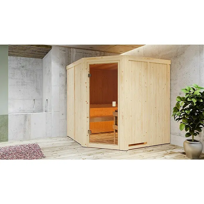 Karibu Elementsauna Kotka - Ohne Ofen, L x B x H: 196 x 196 x 198 cm - Eine helle Holzsauna mit Glastür steht in einem modern gestalteten Raum, neben einer Zimmerpflanze und einem Teppich.