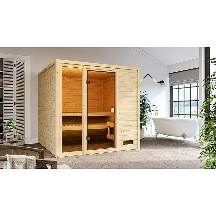 Karibu Massivholzsauna Jutta - L x B x H: 196 x 196 x 187 cm, Ohne Ofen, Ohne Dachkranz - Ein hölzernes Saunahaus mit Glasfront steht in einem Badezimmer. Der Raum ist hell und modern eingerichtet.