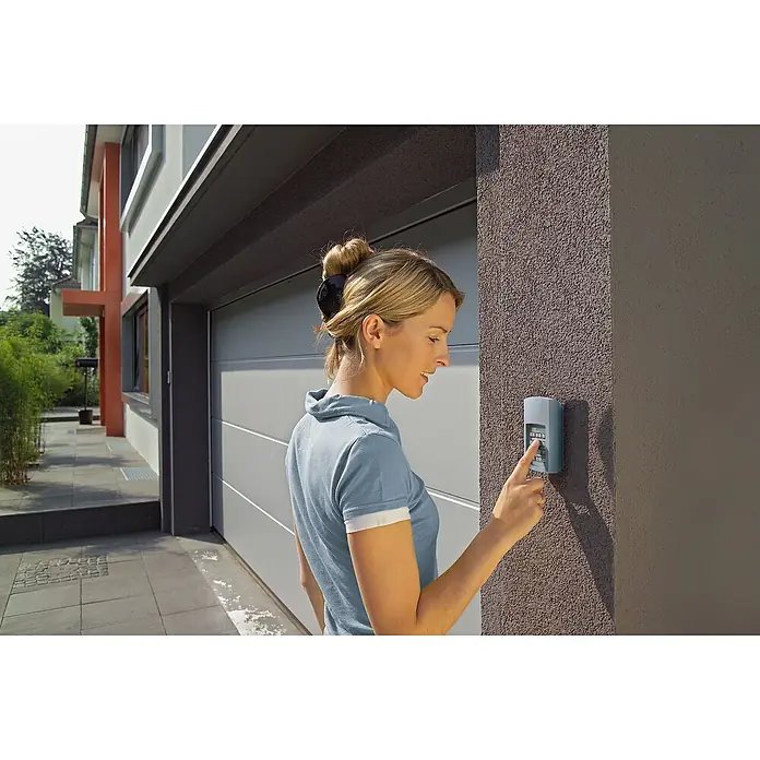 Hörmann EcoStar Funk-Codetaster RCT 3b BiSecur - Aufputzmontage - Eine Frau bedient ein Tastenfeld, das an einer Garagenwand befestigt ist, um das Tor zu öffnen. Der Fokus liegt auf dem Tastenfeld.