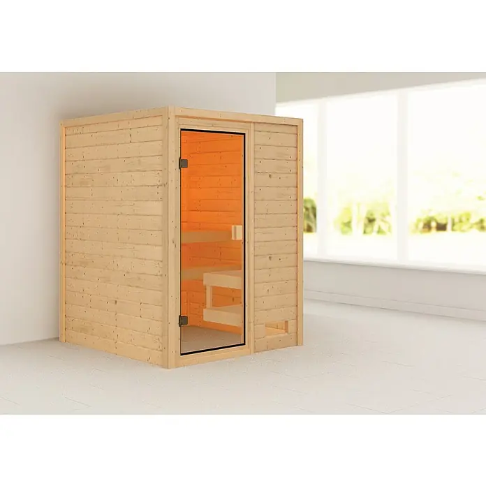 Karibu Massivholzsauna Sandra - L x B x H: 145 x 145 x 187 cm, Ohne Dachkranz, Inklusive Ofenschutzgitter - Ein Panoramabild einer holzverkleideten Sauna mit Glastür, die Wärme und Entspannung in einem modernen Interieur verspricht.