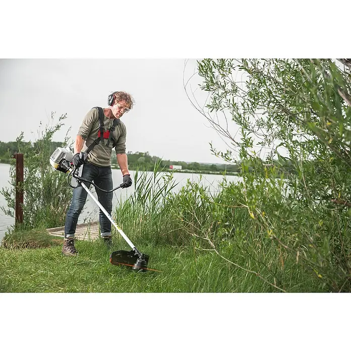 AL-KO Premium Benzin-Motorsense BC 500 B - 1.900 W, Schnittbreite Faden: 41 cm, Schnittbreite Messer: 25,5 cm - Ein Mann trimmt Gras mit einem Rasentrimmer der Marke. Der Trimmer ist mit einem Tragegurt versehen, und der Mann trägt Schutzkleidung.