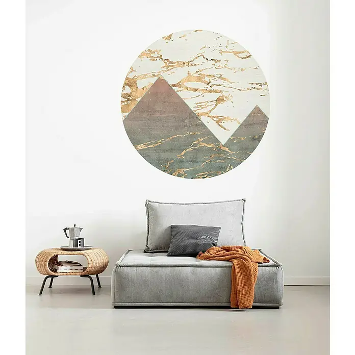 Komar Dots Fototapete rund Precious Peaks - 125 cm, Selbstklebend - Ein modernes Wohnzimmer mit einem grauen Sessel, einem Beistelltisch und einem Wandbild mit Bergmotiv in Gold.