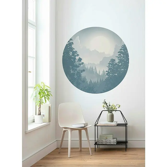 Komar Dots Fototapete rund Blue Valley - 125 cm, Selbstklebend - Wandbild mit Waldmotiv in einem modernen Wohnzimmer. Das runde Bild in Blau- und Grautönen hängt über einem weißen Stuhl und einem Beistelltisch.