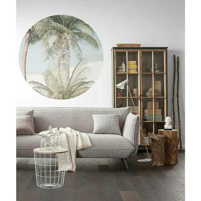 Komar Dots Fototapete rund Hush - 125 cm, Selbstklebend - Wohnzimmer mit grauem Sofa, rundem Wandbild mit Palmen, Vitrinenschrank, Beistelltisch mit Glasflaschen und Holzhocker.