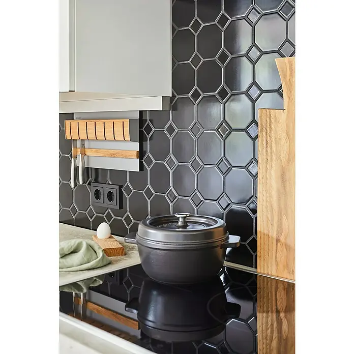 Mosaikfliese Octa G 940N - 30 x 30 cm, Schwarz, Matt - Nahaufnahme einer schwarzen Kochtopf auf einem Induktionskochfeld mit schwarzen Fliesen im Hintergrund und Holzelementen.