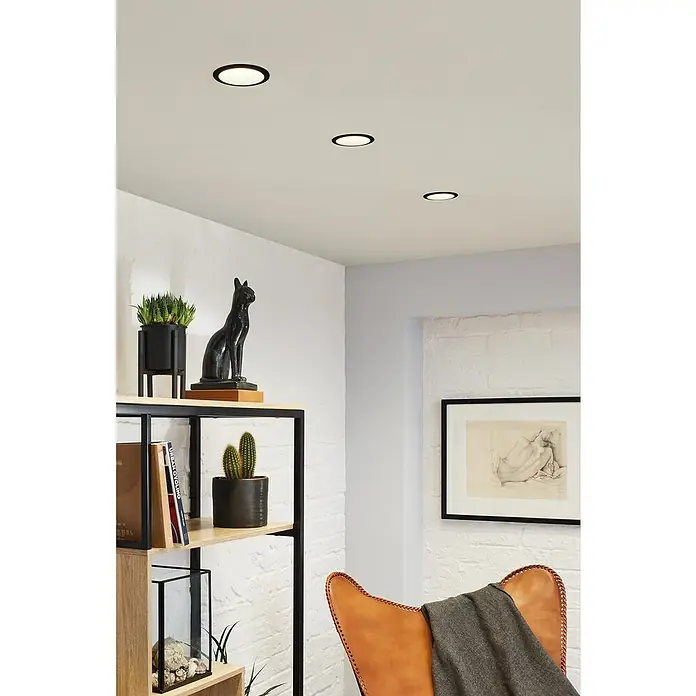 Paulmann LED-Einbauleuchte Cole - 19,5 W, Schwarz/Silber, Warmweiß, 3 Stk. - Innenaufnahme eines Raumes mit Deckenspots, Regal und Sessel.