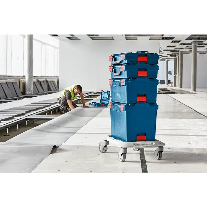 Bosch Professional Systemkoffer L-Boxx 374 - L x B x H: 357 x 442 x 389 mm, ABS - Werkzeugkisten von Bosch auf einem Rollbrett in einer Baustelle mit einem Bauarbeiter.