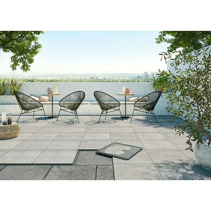 Terrassenfliese Click and Go Portland Grey - 60 x 60 cm, Betongrau, Matt - Eine stilvolle Terrasse mit grauen Fliesen, die teilweise offen liegen, und modernen Sitzmöbeln lädt zum Verweilen im Freien ein.