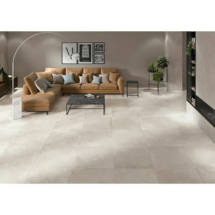BHS Showroom Pavimento porcelánico Lorraine - 60 x 60 cm, Arena, Rectificado - Esta imagen muestra una sala de estar moderna con baldosas de piso claras, un sofá marrón y muebles minimalistas. Las baldosas añaden un toque elegante a la habitación.