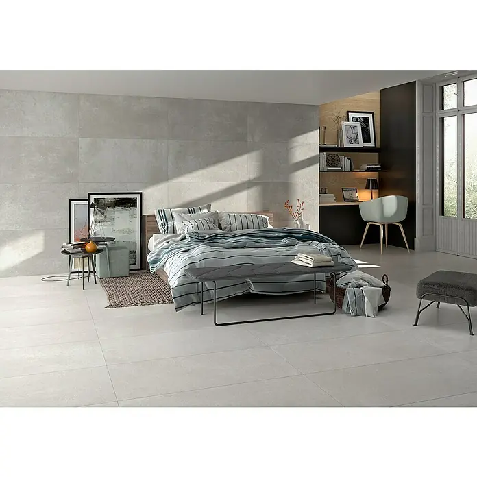 BHS Showroom Pavimento porcelánico Rodano - 120 x 60 cm, Gris oscuro, Rectificado - Dormitorio con grandes baldosas grises, una cama con ropa de cama a rayas y una zona de trabajo al fondo. Ambiente luminoso y moderno.
