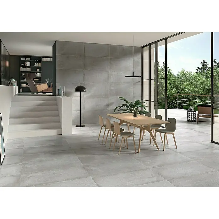 BHS Showroom Pavimento porcelánico Stoneage Soft - 120 x 60 cm, Concreto, Rectificado - Interior espacioso con baldosas de suelo grises de gran formato, una mesa de comedor con sillas y una zona de estar acogedora.