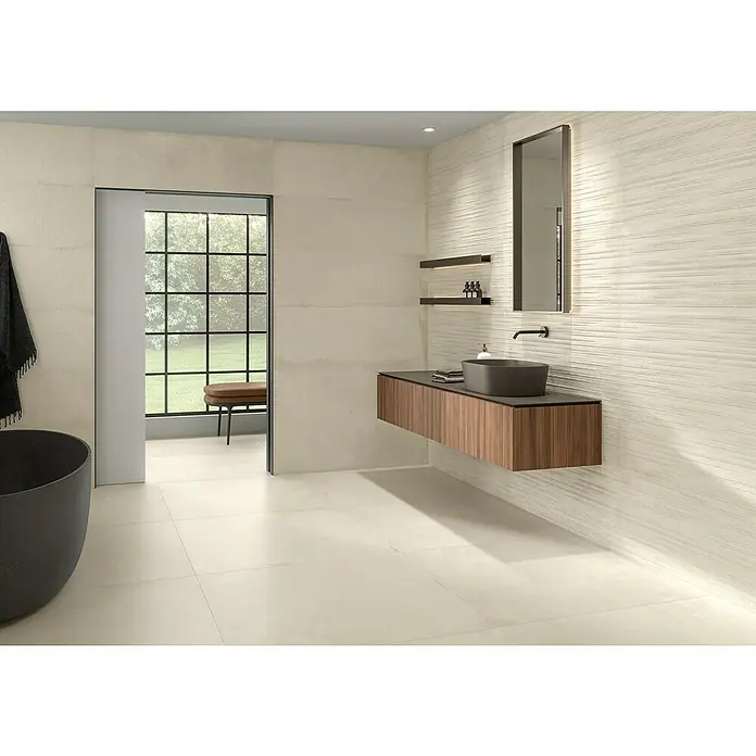 BHS Showroom Pavimento porcelánico Stoneage Soft - 100 x 100 cm, Arena, Rectificado - Elegante baño con moderno mueble de madera, espejo elegante y bañera gris. Los azulejos de colores claros crean un ambiente sereno.