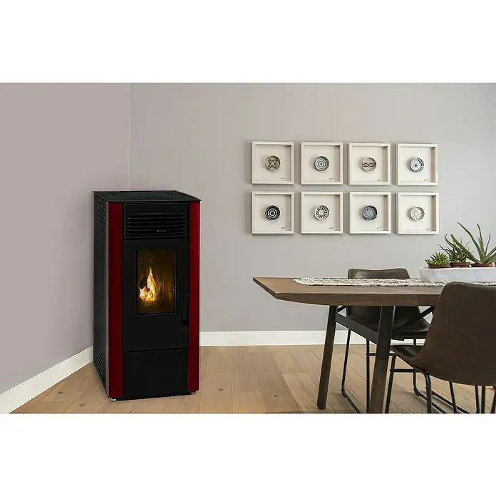 Estufa de pellets Nueva King 10 - 8,61 kW, Volumen de calefacción: 185 m³, 0,9 kg/h - 1,9 kg/h, Burdeos/Negro - Esta imagen muestra una estufa de pellets roja y negra en una habitación, combinando calidez y estilo, rodeada de una decoración moderna con una mesa de madera y arte mural.