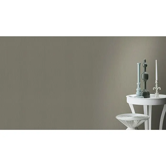 Rasch BARBARA Home Collection II Vliestapete - Grau/Oliv, Uni, 10,05 x 0,53 m - Drei dekorative Kerzenhalter und ein weißer Beistelltisch vor einem grauen Hintergrund mit subtiler Textur verleihen jedem Raum Eleganz.