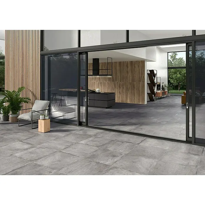 BHS Showroom Pavimento porcelánico Stoneage Soft - 60 x 60 cm, Ceniza, Rectificado - Zona de patio con baldosas de suelo antracita modernas, una disposición de asientos elegante y vegetación exuberante, creando un ambiente acogedor.