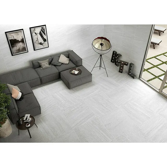 BHS Showroom Pavimento porcelánico Carleen - 75 x 37 cm, Blanco, Rectificado - Un salón moderno con baldosas de color gris claro, un sofá gris y una decoración elegante. Las baldosas son el punto destacado.