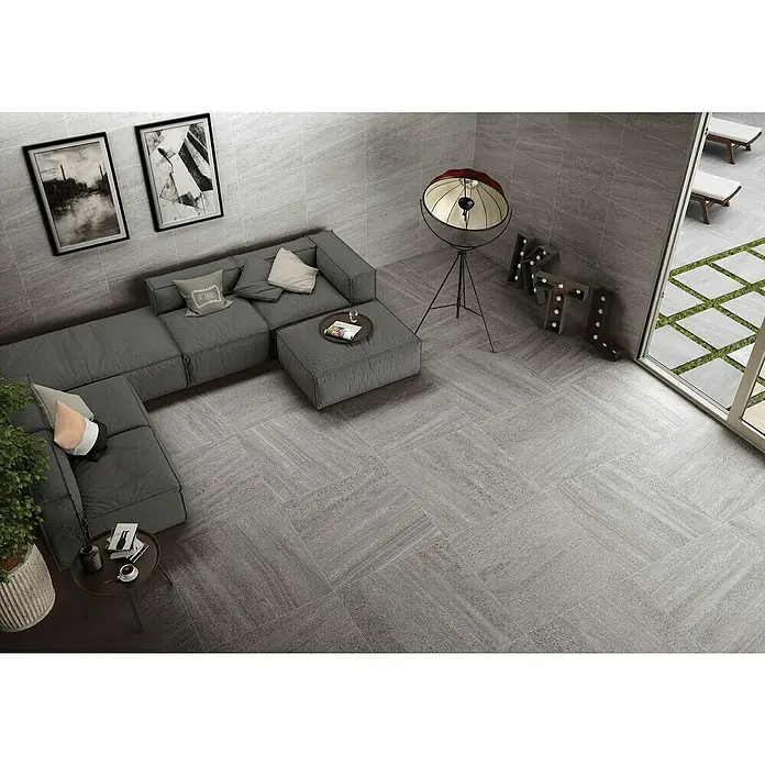 BHS Showroom Pavimento porcelánico Carleen - 75 x 37 cm, Gris, Rectificado - Baldosas de suelo grises con diseño texturizado, que complementan un interior de sala de estar moderna con sofá y elementos decorativos.