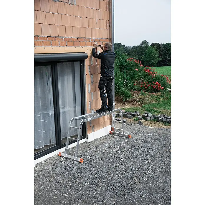 Krause Monto Gelenkleiter-Plattform - L x B: 142 x 30 cm - Mann arbeitet an einer Hauswand mit einer Klappleiter. Die Klappleiter ist silberfarben und hat orangefarbene Füße. Er trägt Arbeitskleidung.