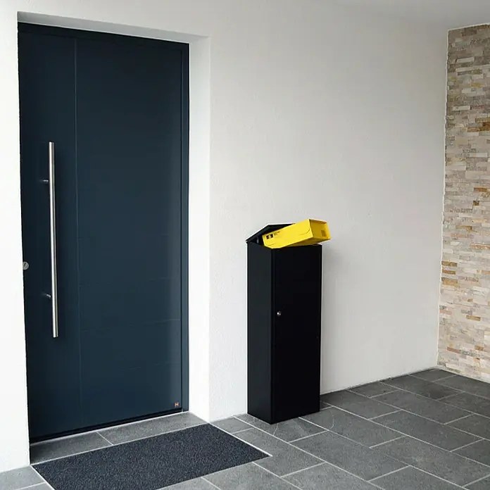 Rottner Paketbox Parcel Keeper - L x B x H: 23 x 38 x 105 cm, Schwarz, Edelstahl, Paketfach - Moderne Haustür in dunklem Anthrazit mit langem, senkrechtem Griff und einem schwarzen Briefkasten mit gelbem Paket.