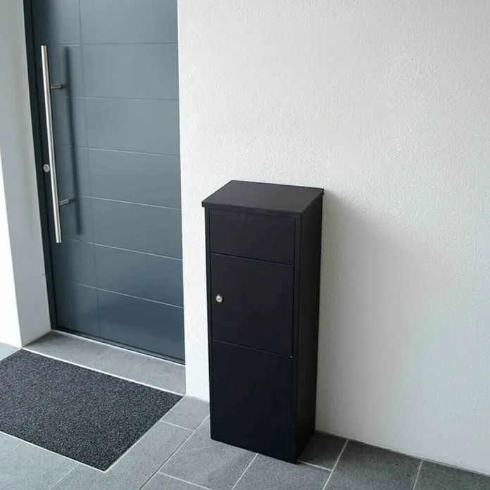 Rottner Paketbox Parcel Keeper - L x B x H: 23 x 38 x 105 cm, Schwarz, Edelstahl, Paketfach - Das Bild zeigt einen modernen, schwarzen Briefkasten neben einer Haustür. Der Briefkasten ist schlicht und funktional gestaltet.