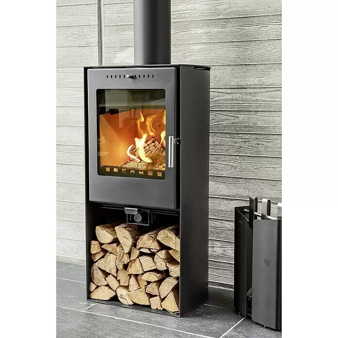 Aduro Kaminofen 19 - 5 kW, Raumheizvermögen: 350 m³, Material Verkleidung: Stahl, Schwarz - Moderner schwarzer Holzofen mit sichtbaren Flammen durch die Glastür und gestapeltem Holz im unteren Fach, vor einer Holzpaneelwand.