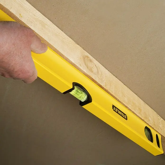 Stanley Nivel de burbuja STHT1-43103 - Aluminio, Amarillo, 60 cm - Una persona utiliza un nivel de burbuja Stanley amarillo para alinear un trozo de madera al techo. Precisión en proyectos de construcción.