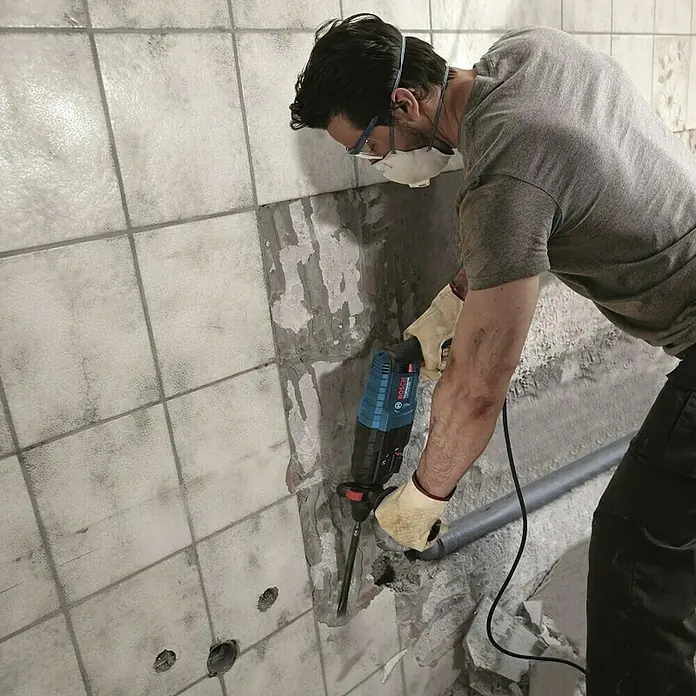 Bosch Professional Kombihammer GBH 240 - 790 W, 2,7 J, SDS-Plus-Aufnahme - Ein Mann entfernt Fliesen mit einem Bosch-Hammer, Schutzbrille und Maske tragend.
